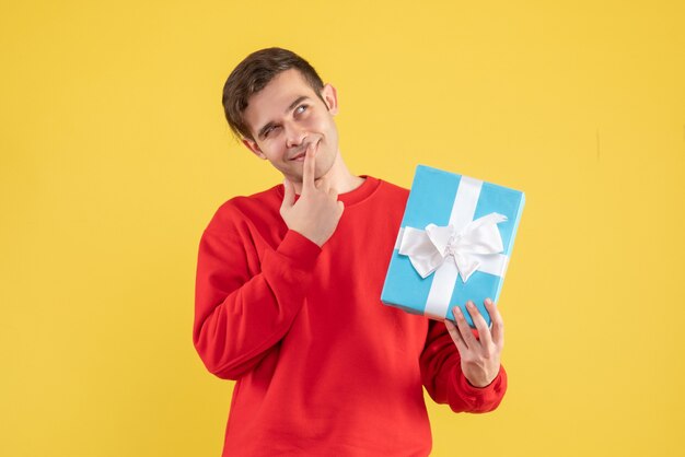 Front view thinking young man with red sweater standing on yellow background