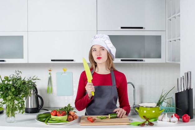 Front view thoughtful female cook in apron holding knife