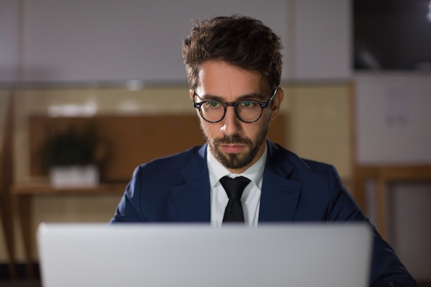 Vista frontale dell'uomo premuroso in occhiali che esaminano computer portatile