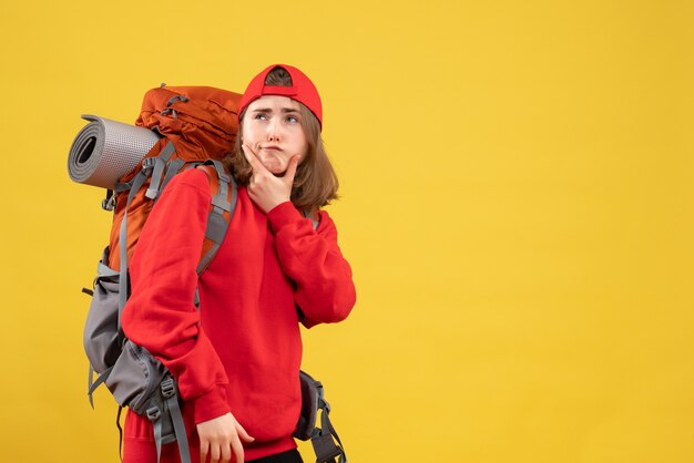 黄色の壁に立っている赤いバックパックの正面図思慮深い旅行者の女性