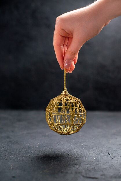 Front view thread string golden xmas tree ball in female hand on dark isolated background