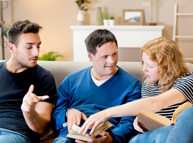 Вид спереди трех друзей, чтение на диване у себя дома