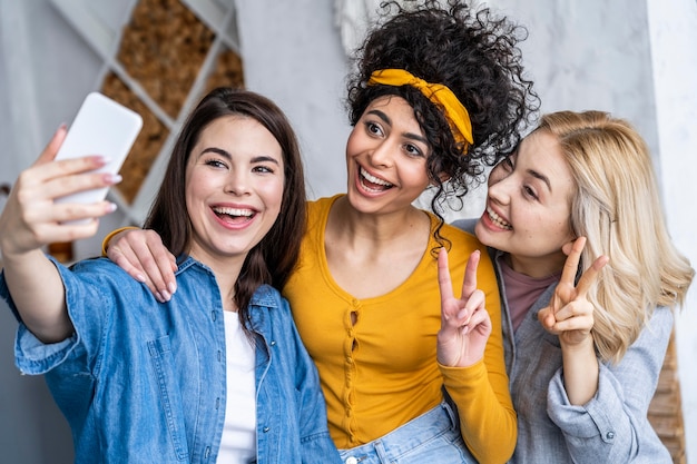 Front view of three happy women laughing and taking selfie