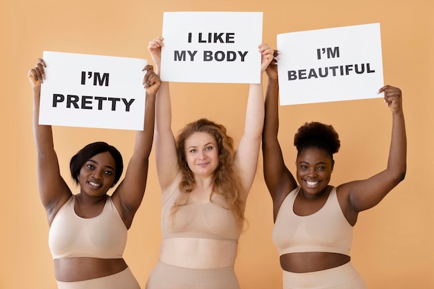 Front view of three women holding placards with body positivity statements