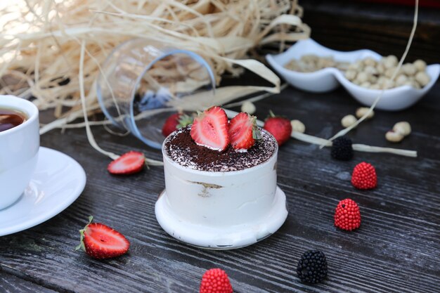 Front view tiramisu in a cup with strawberries on the table