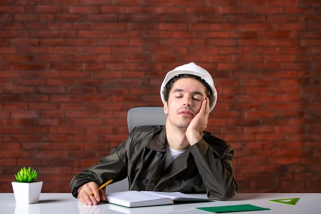 Front view tired male engineer sitting behind his working place document plan job business corporate contractor agenda property builder