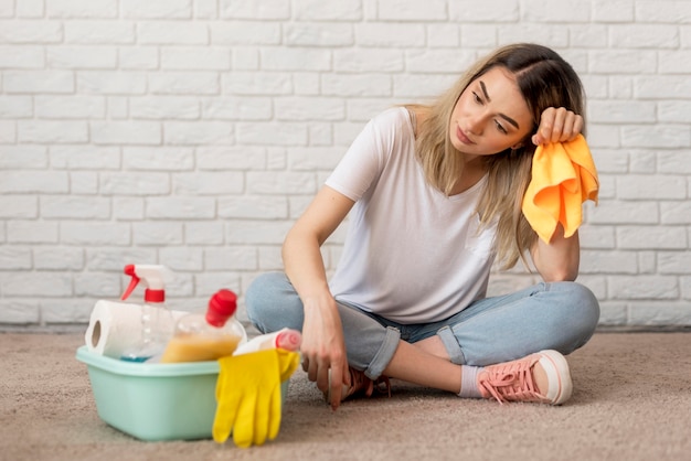 Front view of tired woman with cleaning supplies and cloth