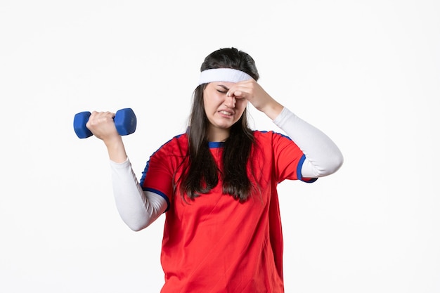 Front view tired young female in sport clothes working out with dumbbells