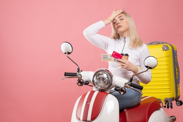 Front view tired young lady on moped putting hand on her head holding coffee cup