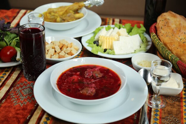 Вид спереди традиционное украинское блюдо борщ в тарелке с сыром и хлебом тандыр с стаканом водки и сока на столе