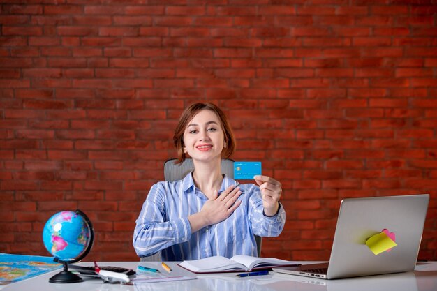 Front view travel agent behind her working place holding credit card map indoors manager operator worker agency document service money world