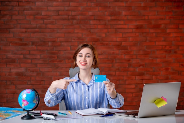 Front view travel agent behind her working place holding credit card map indoors manager service money world occupation worker agency operator