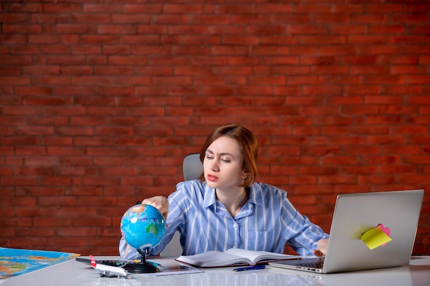 Front view travel agent behind her working place working with laptop and observing globe map assistant agency indoors operator service manager