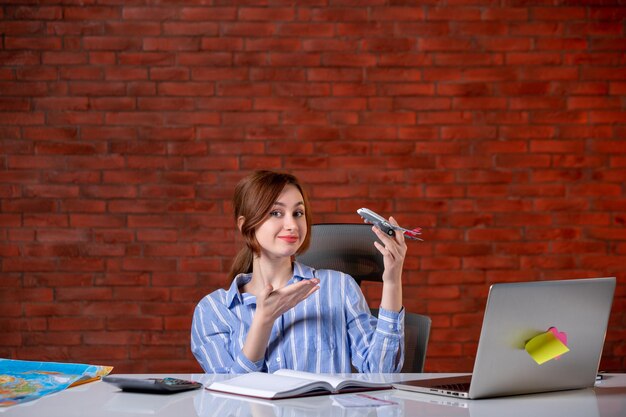 Front view travel agent sitting behind her working place holding toy plane agency service world operator assistant map global ticket managers