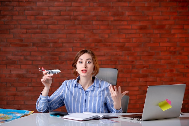 Front view travel agent sitting behind her working place playing with toy plane agency service assistant manager map operator global world ticket