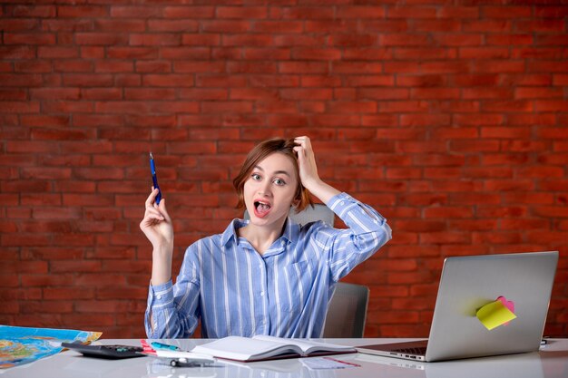 Front view travel agent sitting behind her working place with laptop and notepad indoors map agency service global assistant ticket world