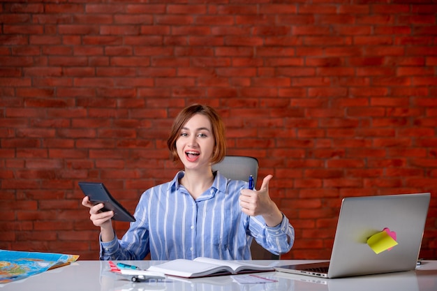 Front view travel agent sitting behind her working place with laptop working with calculator map agency service manager assistant ticket world global