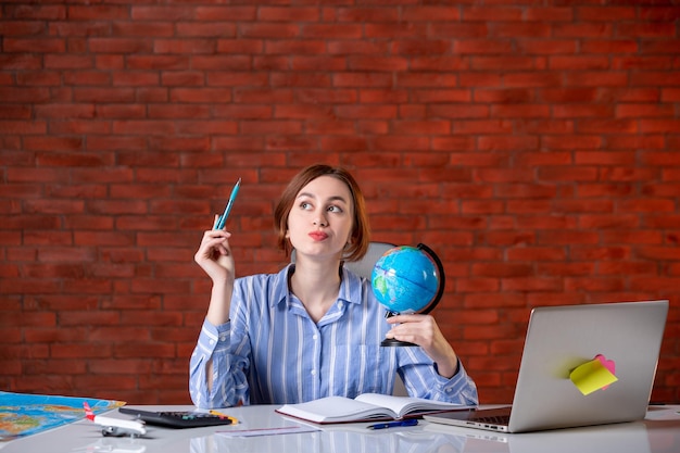 Front view travel agent sitting behind her working place with little globe assistant agency map indoors operator service world managers