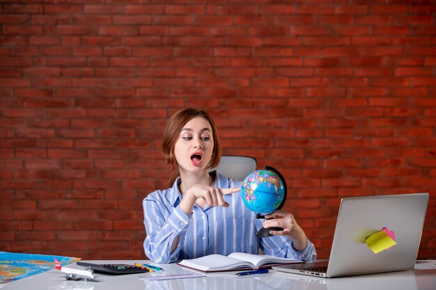 Front view travel agent sitting behind her working place with little globe map assistant agency world manager indoors operator service