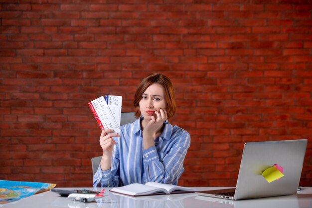 Front view travel agent sitting behind her working place with plane tickets agency service global manager assistant world map operator