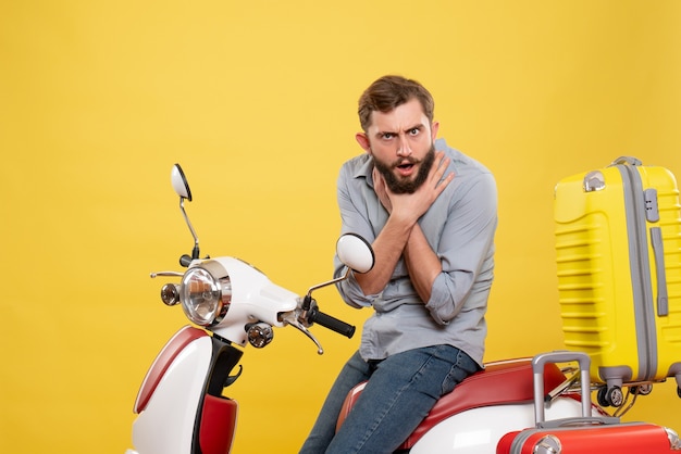 Front view of travel concept with exhausted young man sitting on motocycle with suitcases on it suffocating himself on yellow 