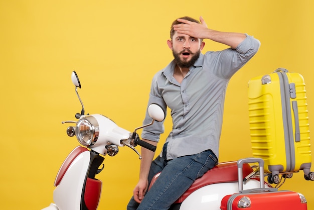 Front view of travel concept with exhausted young man sitting on motocycle with suitcases on it on yellow 