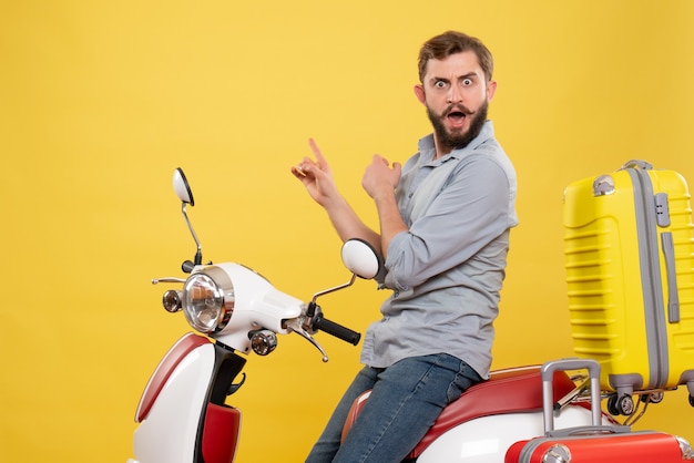 Front view of travel concept with nervous angry emotional young man sitting on motocycle with suitcases on it on yellow 