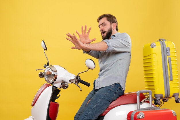 Вид спереди концепции путешествия с испуганным молодым человеком, сидящим на мотоцикле с чемоданами на нем на желтом