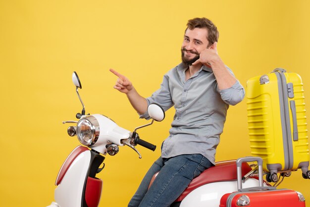 Вид спереди концепции путешествия с улыбающимся молодым человеком, сидящим на мотоцикле с чемоданами на нем, делая жест на желтом «позвони мне»