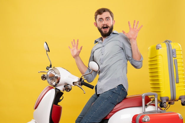 Front view of travel concept with young man sitting on motocycle with suitcases feeling nervous on it on yellow 