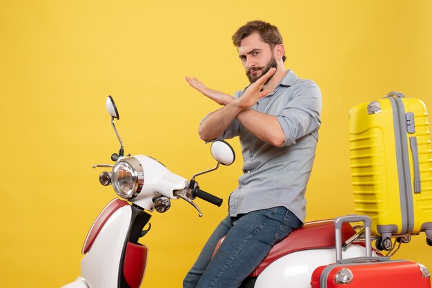 Вид спереди концепции путешествия с молодым человеком, сидящим на мотоцикле с чемоданами, делая жест остановки на нем на желтом