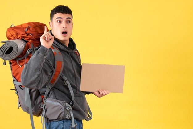 Front view traveler man with backpack holding cardboard pointing at ceiling