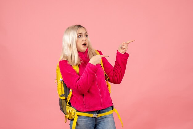 Front view traveler woman in casual clothes wearing backpack pointing at right