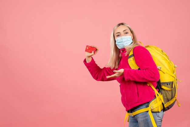 Front view traveler woman with backpack wearing mask holding card