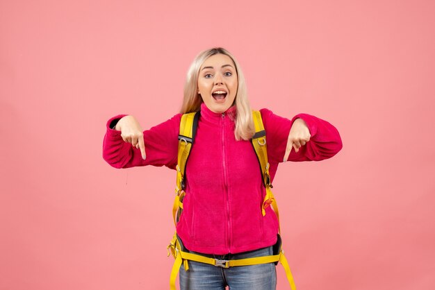 Front view traveler woman with yellow backpack pointing with fingers down