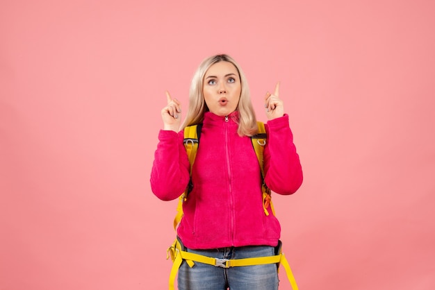 Front view traveler woman with yellow backpack pointing with fingers up