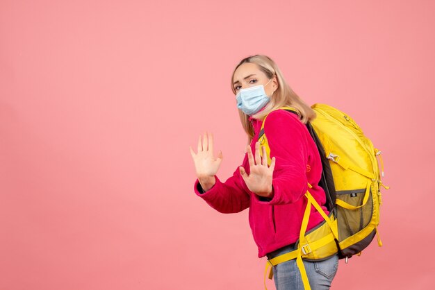 Front view traveler woman with yellow backpack wearing mask gesturing stop sign