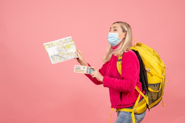 Front view traveler woman with yellow backpack wearing mask holding map and ticket