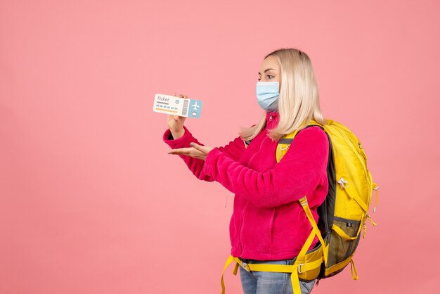 Front view traveler woman with yellow backpack wearing mask holding ticket