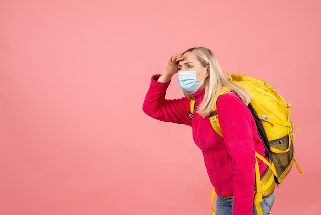 Front view traveler woman with yellow backpack wearing mask looking at something