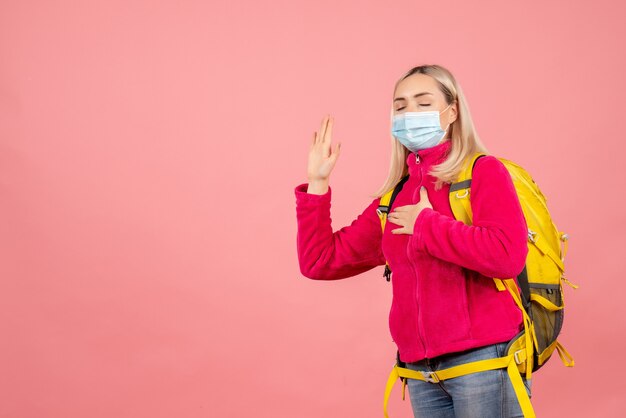 Front view traveler woman with yellow backpack wearing mask promising with closed eyes