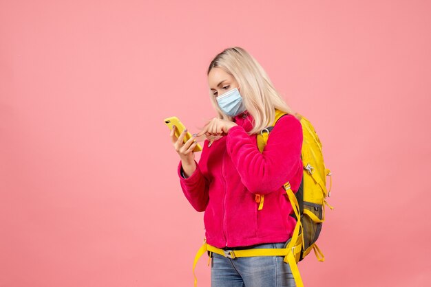 Женщина-путешественница, вид спереди с желтым рюкзаком в маске, разговаривает по телефону