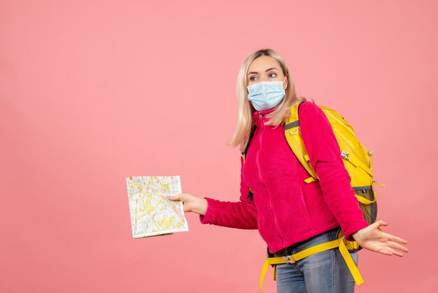 Front view traveler woman with yellow backpack wearing medical mask holding map