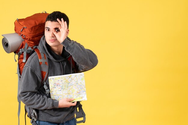 Front view traveller man with backpack holding map holding up okay sign in front of his eye