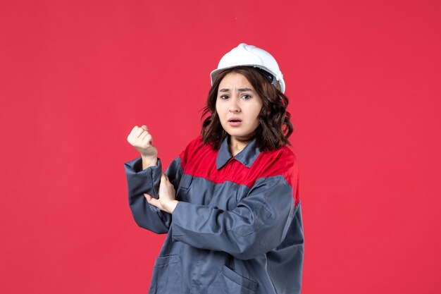 Вид спереди беспокоящей женщины-строителя в униформе с каской и страдающей от боли в руке на изолированном красном фоне