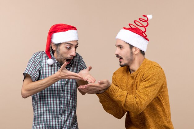 베이지 색 격리 된 배경에 그의 손에 다른 뭔가를 보여주는 산타 모자와 전면보기 두 놀란 남자