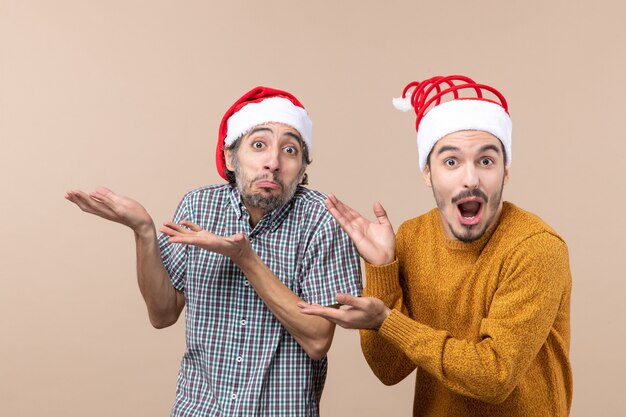 Front view two amazed guys with santa hats showing something beige isolated background