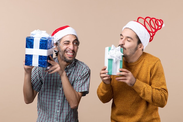 Front view two blissful guys enjoying their christmas presents on beige isolated background