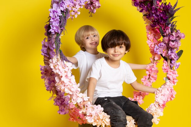 A front view two boys adorable sweet cute sitting on the flower made stand on the yellow floor