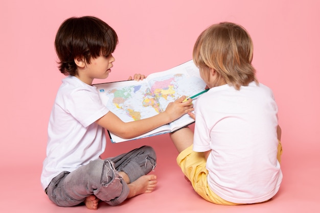 front view two boys drawing maps in white t-shirts on pink floor